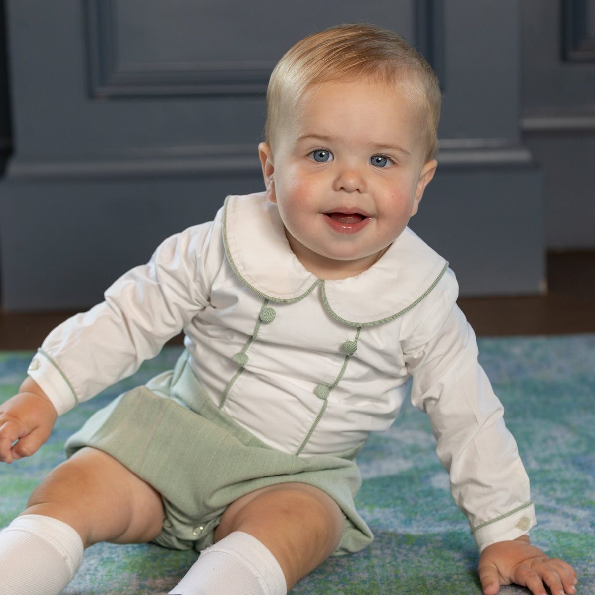 Front of Barrett bubble romper in sage green herringbone on seated baby, showing Peter Pan collar and piped trim