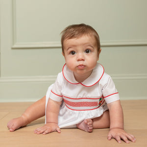 White baby boy holiday bubble with red toy soldier smocking and Peter Pan collar, Henry Duvall's Charlie Bubble in cotton poplin for Christmas celebrations