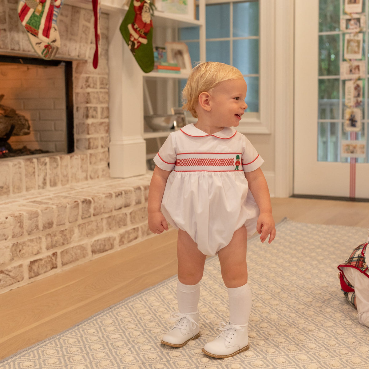 White baby boy holiday bubble with red toy soldier smocking and Peter Pan collar, Henry Duvall's Charlie Bubble in cotton poplin for Christmas celebrations