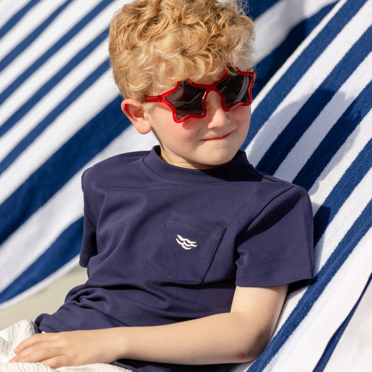 Three-quarter view of boy wearing Tucker Tee in Narragansett Navy showing chest pocket with embroidered wave on striped towel