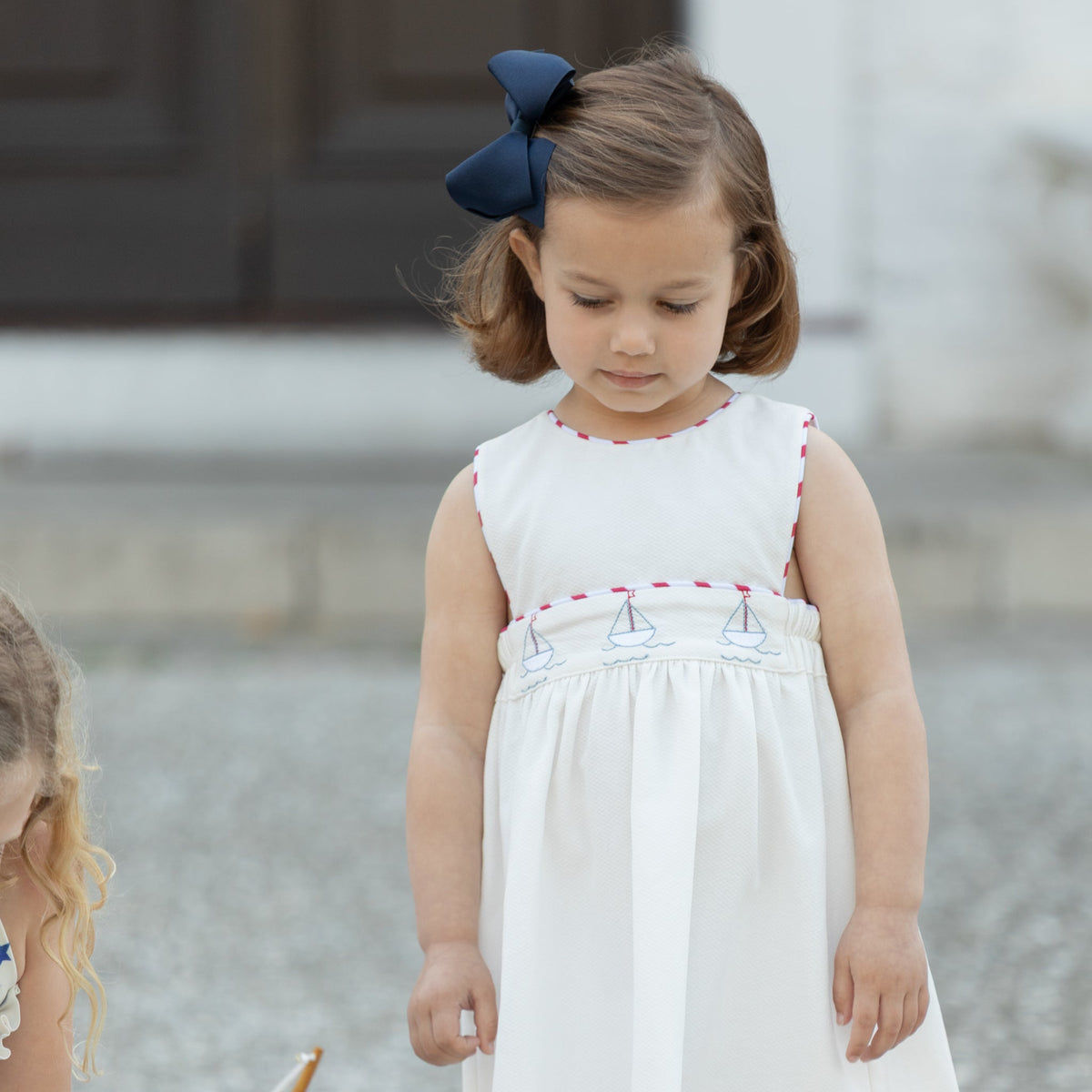 Front view of Leila dress on a toddler showcasing embroidered sailboat smocking with stone steps background