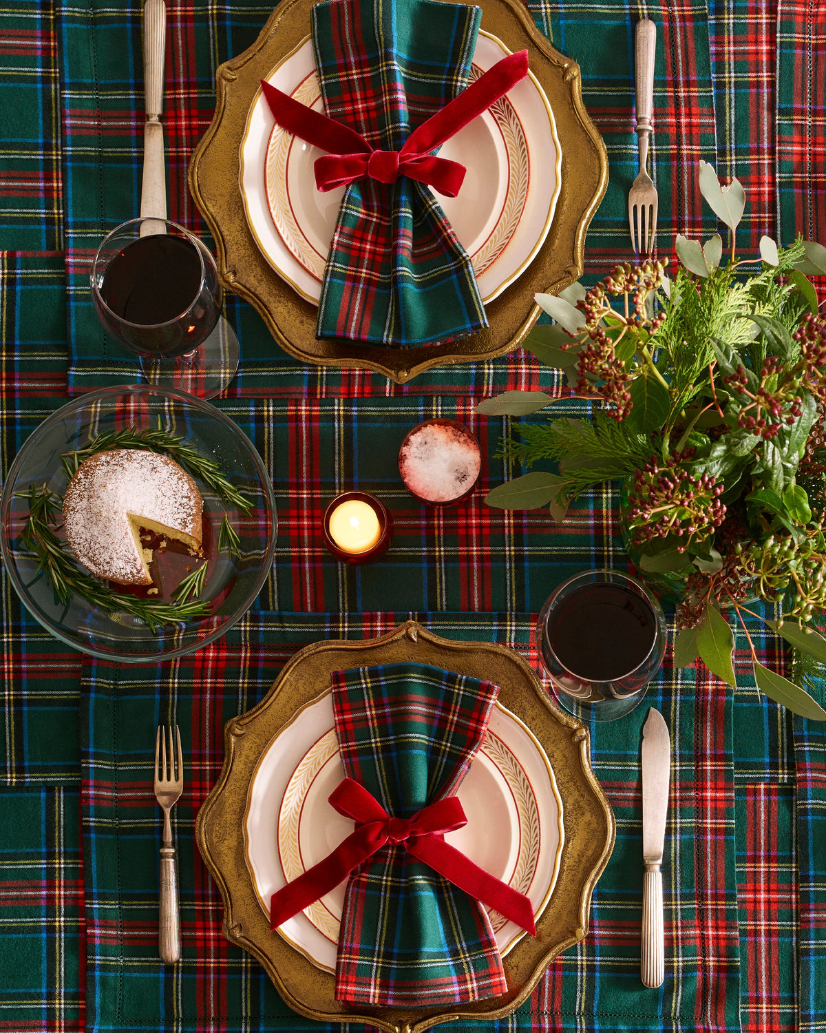 Kensington Tartan placemats dress a festive table with layered plates, silverware, candles, dessert, and greenery