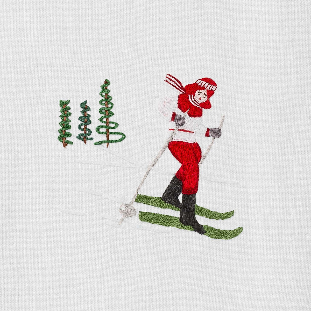 Close-up of Skier Jill towel showcasing red hand-embroidered skier and three green embroidered trees on white cotton background