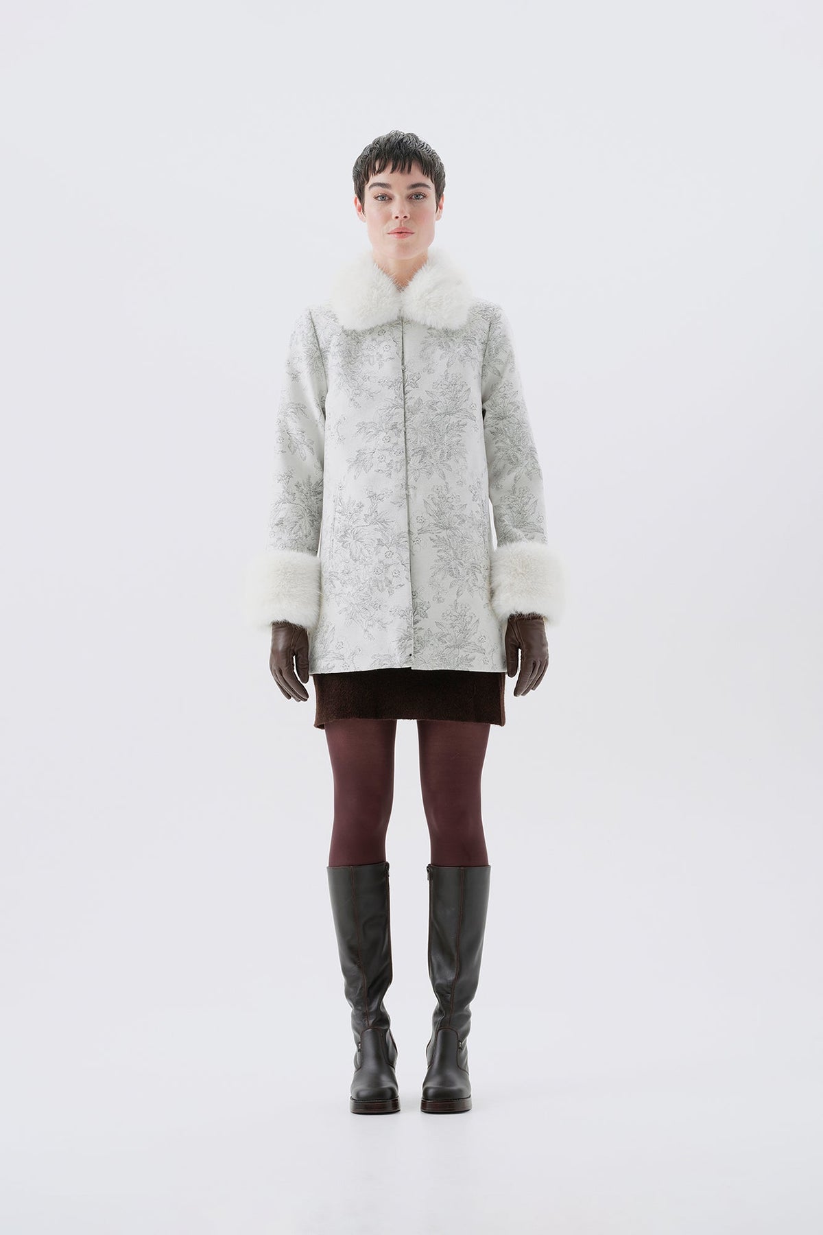 A model viewed from the front wearing a patterned white and grey faux-fur coat with white faux-fur collar and cuffs.