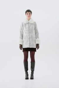 A model viewed from the front wearing a patterned white and grey faux-fur coat with white faux-fur collar and cuffs.
