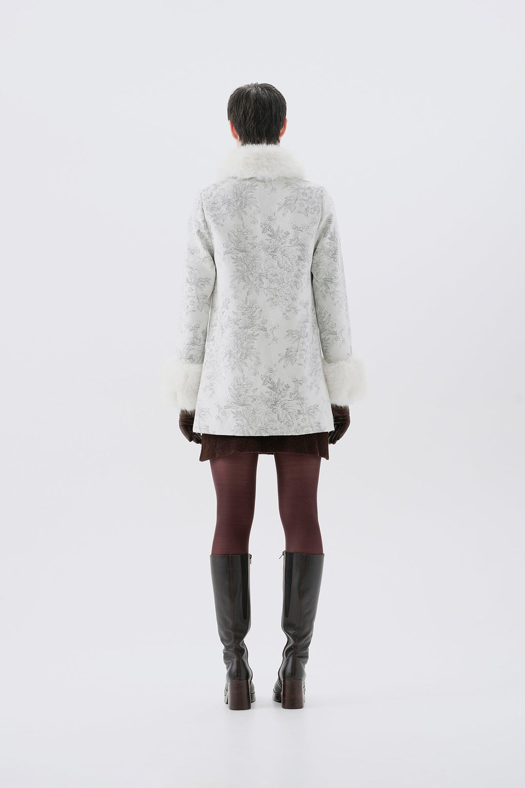 A model viewed from the back wearing a patterned white and grey faux-fur coat with white faux-fur collar and cuffs.