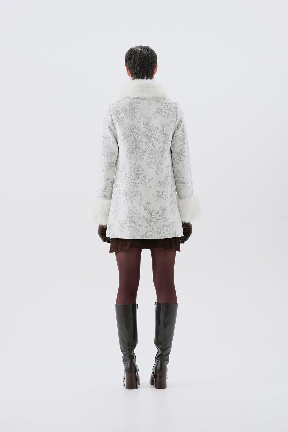 A model viewed from the back wearing a patterned white and grey faux-fur coat with white faux-fur collar and cuffs.