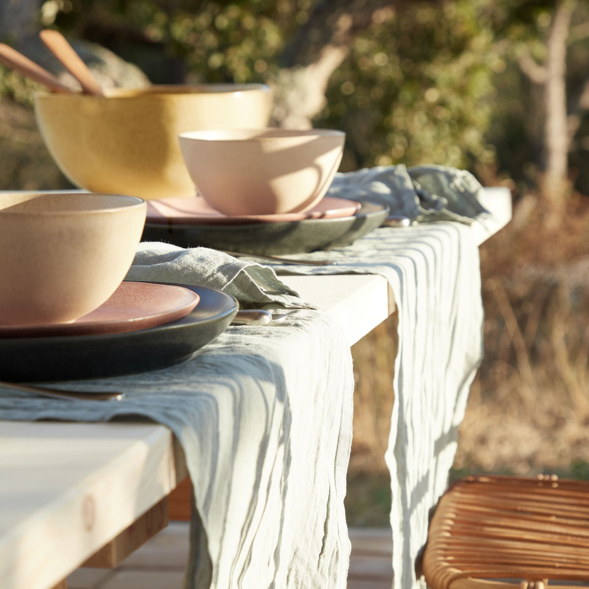Mint linen table runner draped over an outdoor table with layered plates and bowls
