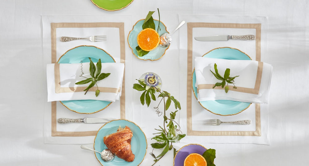 Top-down view of Lowell placemats (set of 4) showing white linen with beige sateen trim on a styled table with turquoise plates and silver flatware
