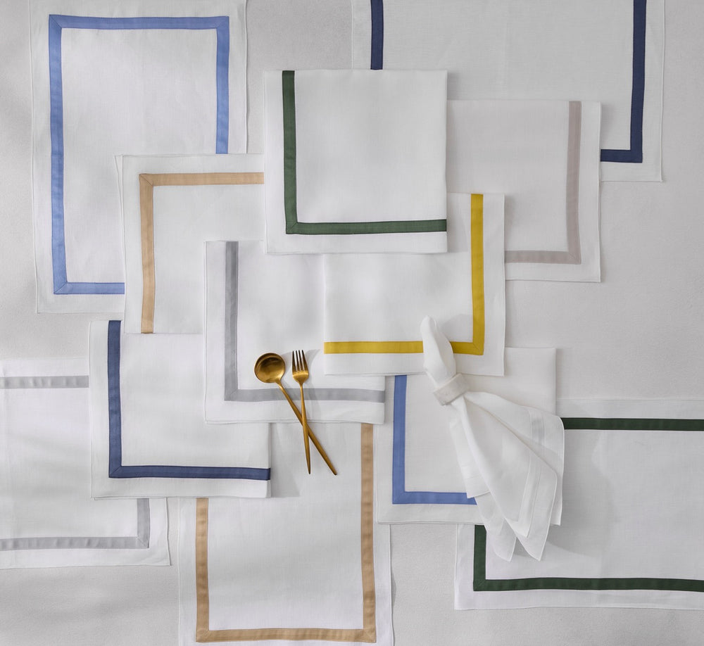 Flat lay of Lowell napkins showing white linen with colored sateen borders and gold flatware on light gray background