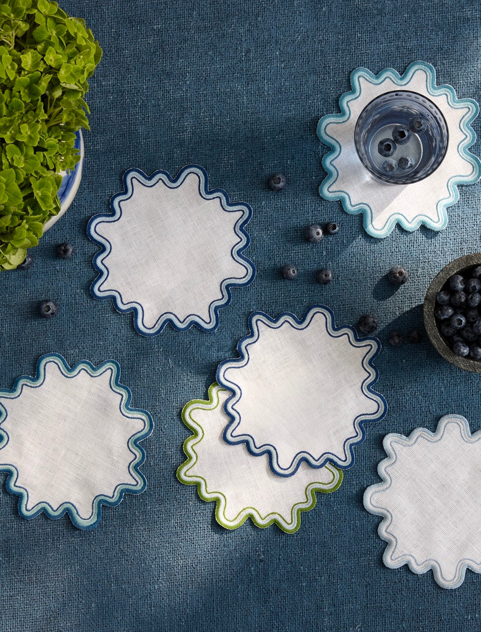 Top view of Wave Cocktail Napkins showcasing wavy two-tone scalloped borders in blue, aqua, and green on a dark blue textured background