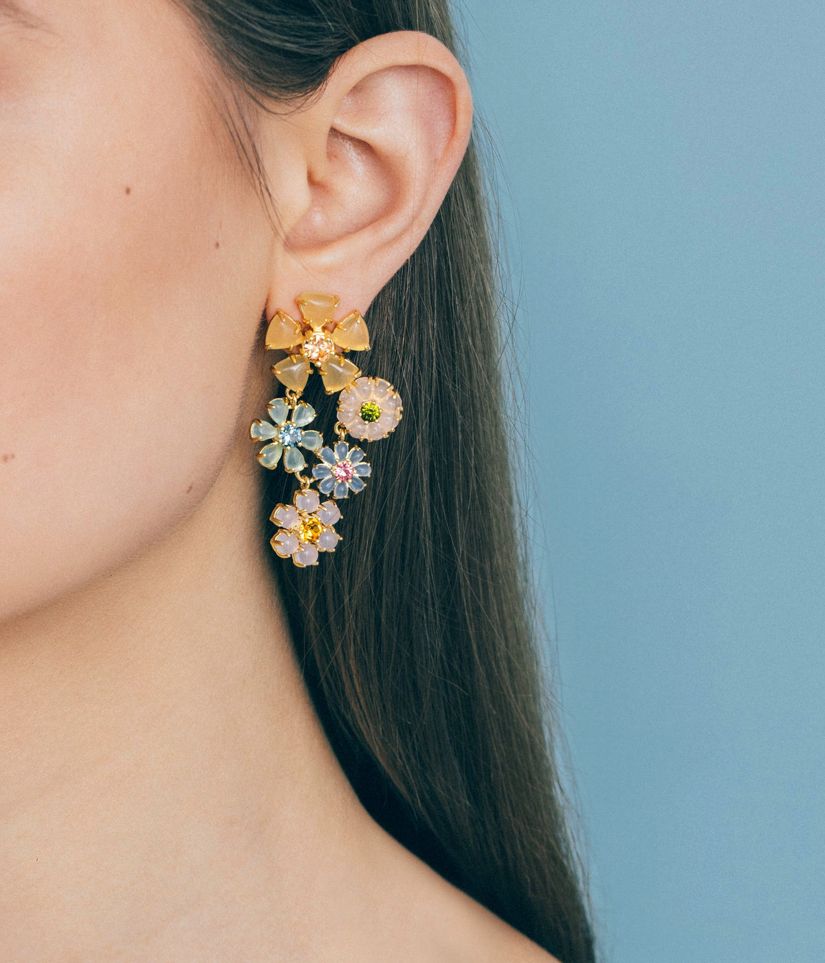 Close-up of Talia Statement earring on ear showing cascading pastel floral crystals and gold finish on pale blue background