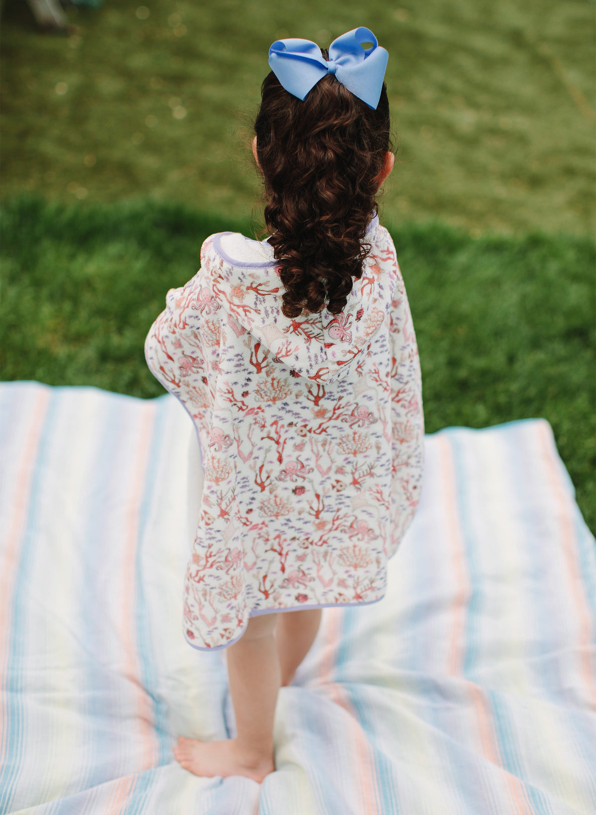Back view of Rosy Coral Reef Swim Poncho showcasing coral reef print and lavender trim on a child outdoors