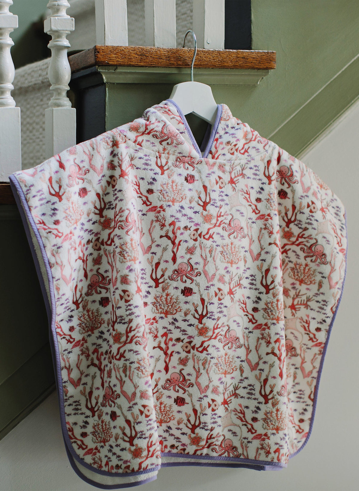 Front view of Rosy Coral Reef Swim Poncho showcasing coral reef print and lavender bias trim on a hanger