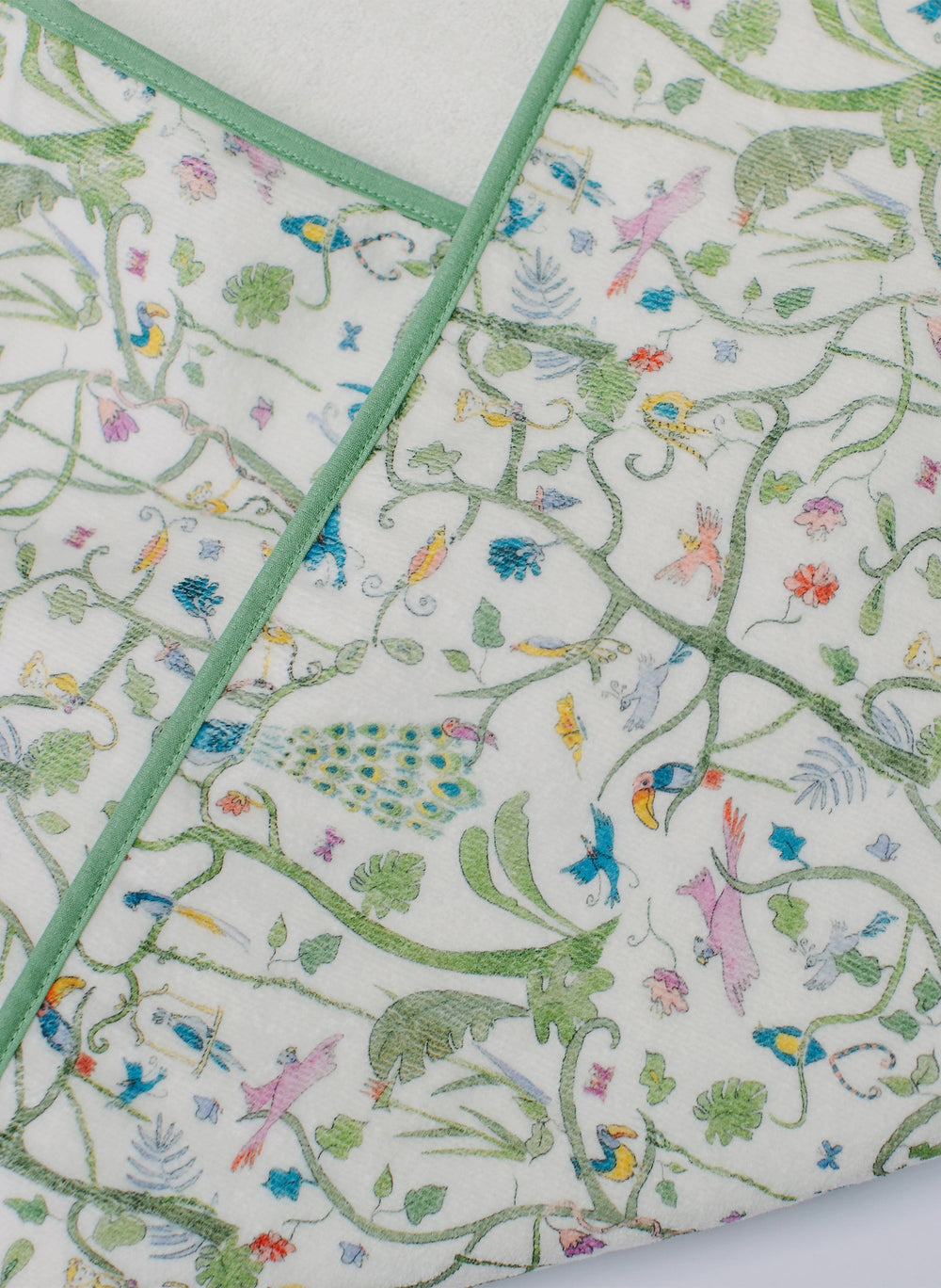 Close-up of Tropical Garden hooded bath towel showing green binding and bird and peacock print on white terry