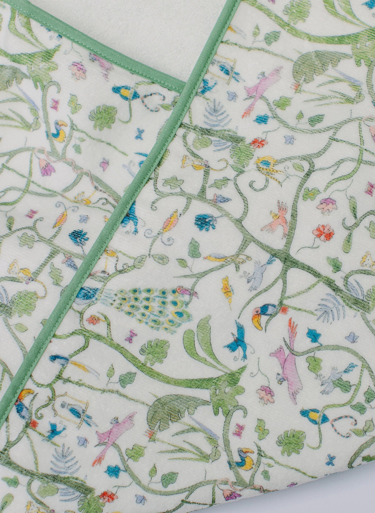 Close-up of Tropical Garden hooded bath towel showing green binding and bird and peacock print on white terry