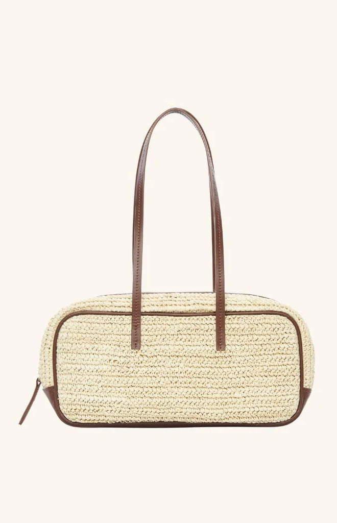 Front view of The Bowler Bag in natural raffia showcasing brown leather trim and long top handles on a pale background