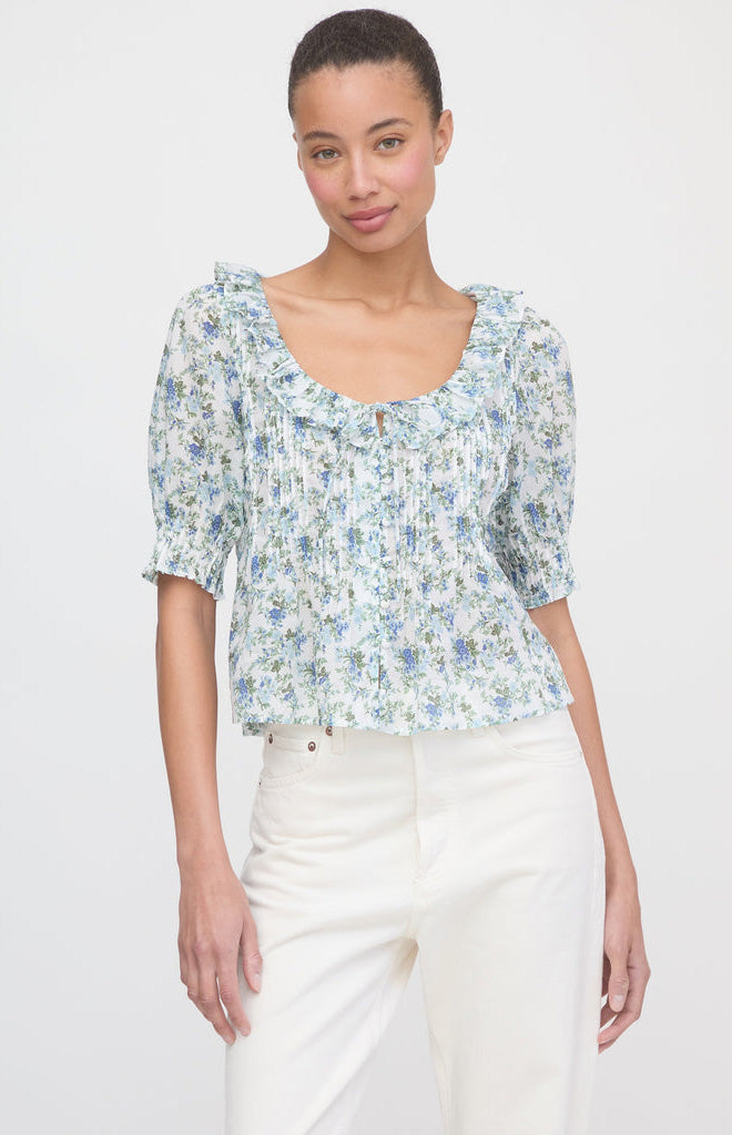 Front view of Camri Top in English Daisy on model, ruffled scoop neck with tie, puff sleeves, blue-green floral print