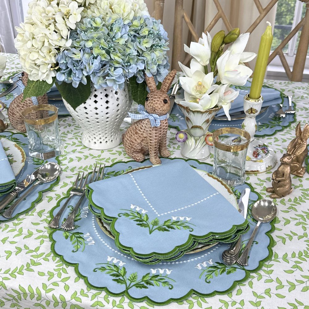 Easter table setting with bunny decorations, floral arrangements, and blue and green plates. Luxury Lilly of the valley placemats