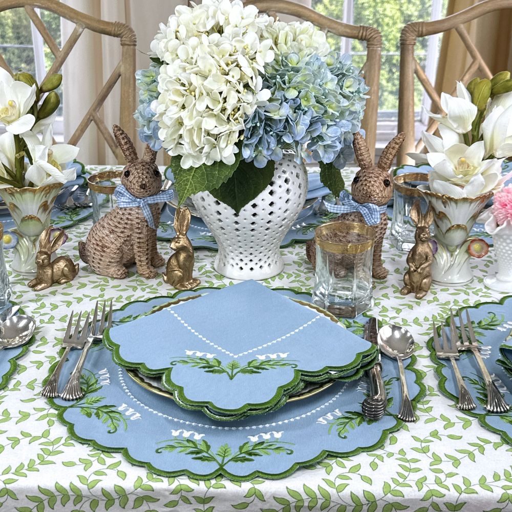 Easter table setting with bunny decorations, floral arrangements, and blue and green plates. Luxury Lilly of the valley placemats