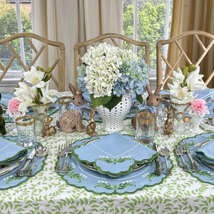 Easter table setting with bunny decorations, floral arrangements, and blue and green plates. Luxury Lilly of the valley placemats