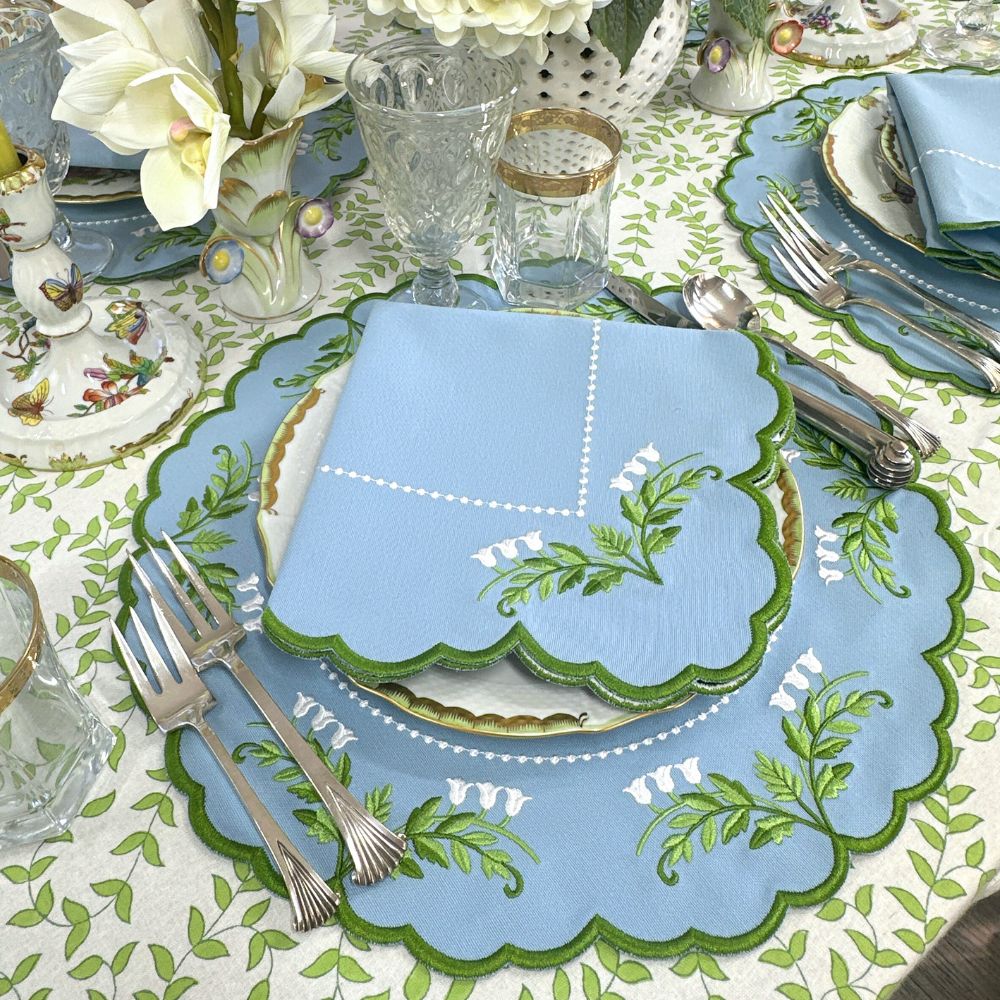 Decorative table setting with a blue placemat featuring green leaf patterns on a patterned tablecloth.
