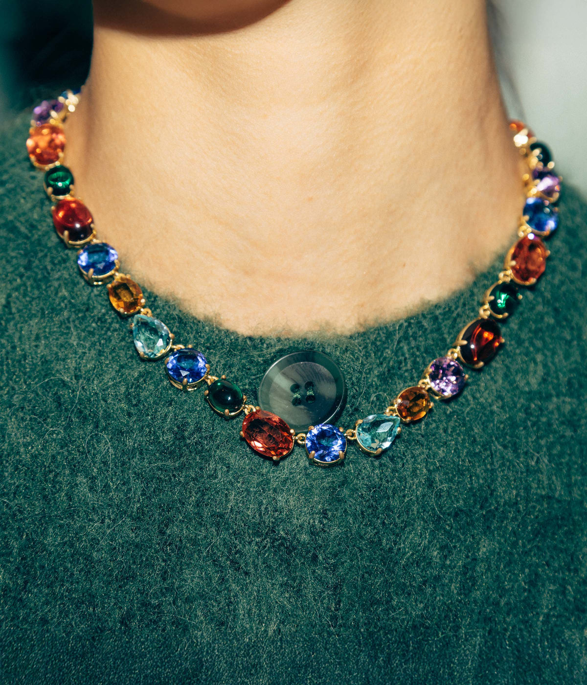 Close-up of Tinsely Necklace on model showcasing multicolored glass stones in gold prong settings against green sweater