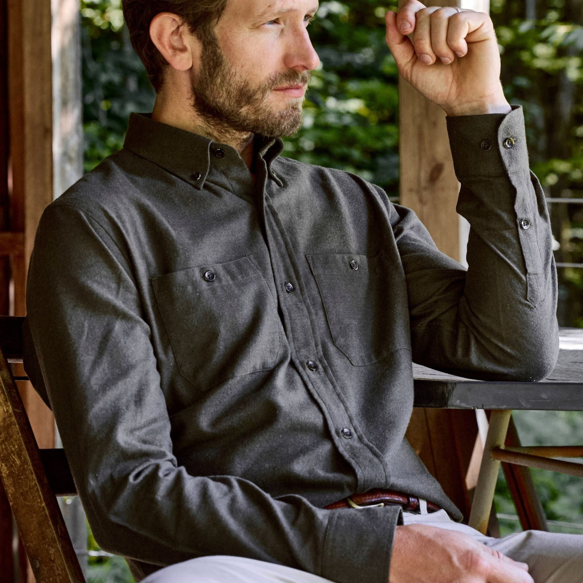 A man in a Tom Beckbe Dixon Brushed Cotton Twill Shirt sits outdoors, resting his arm on the table edge.