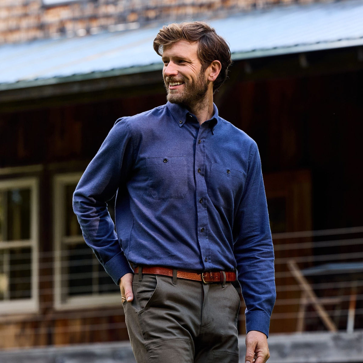 Man wearing Tom Beckbe Dixon Brushed Cotton Twill Shirt and brown pants stands outdoors, smiling with a hand in his pocket.