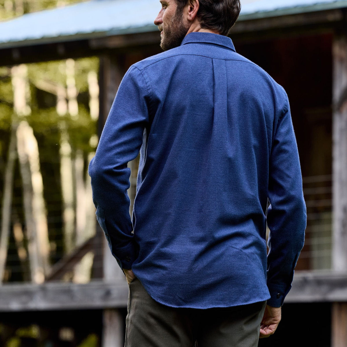 Man outdoors wearing the Tom Beckbe Dixon Brushed Cotton Twill Shirt and olive pants by a wooden building.