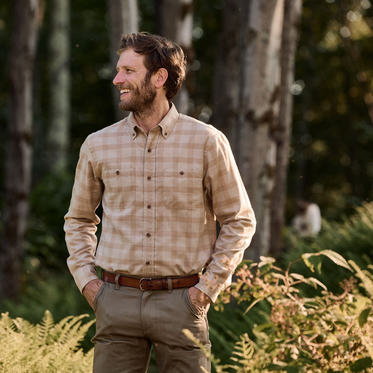 Man standing outdoors among trees, smiling in a Tom Beckbe Dixon Brushed Cotton Twill Shirt and khaki pants.