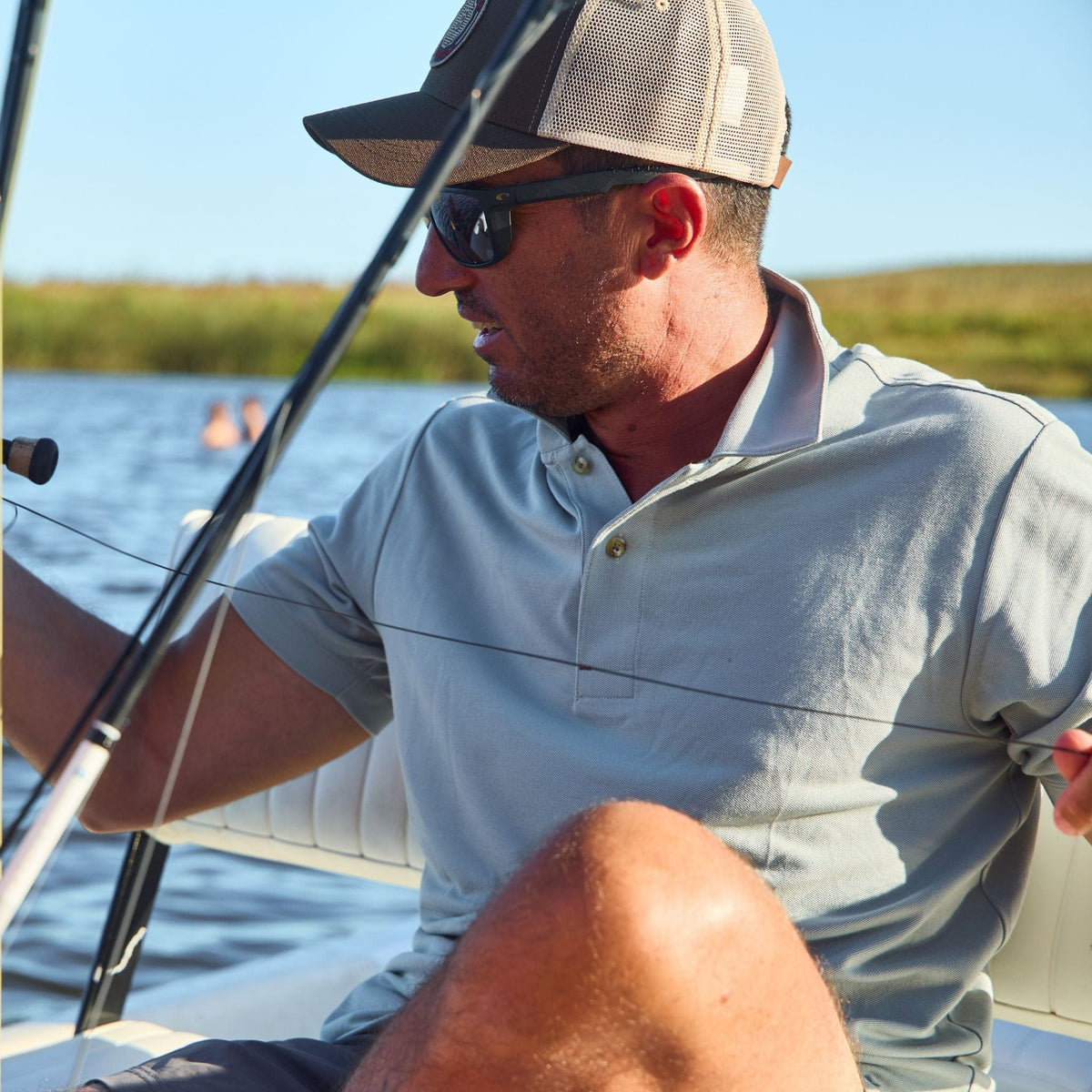 Man on a boat fishing, wearing sunglasses and a moisture-wicking Tom Beckbe Coastal Polo Shirt.