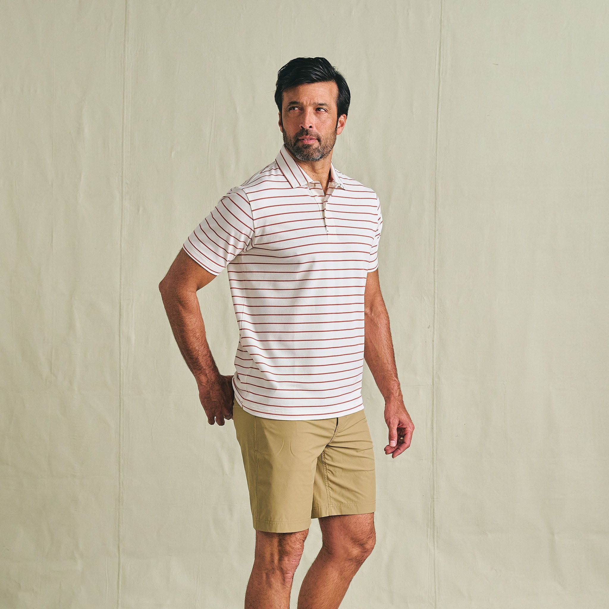Man in Tom Beckbe Crenshaw Performance Short and striped polo stands against a plain background, looking to the side.