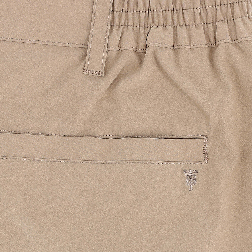Close-up of Tom Beckbe Crenshaw Performance Short in beige, featuring elastic waistband, belt loop, welt pocket, and logo.