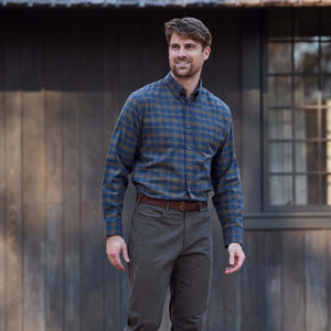 Man wears Tom Beckbe Dixon Brushed Cotton Twill Shirt with olive pants outside a dark wooden building.