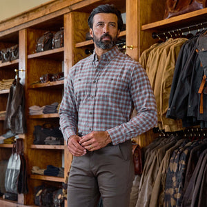 A man wears the Tom Beckbe Dixon Brushed Cotton Twill Shirt and brown pants in a store with jackets and bags on shelves.