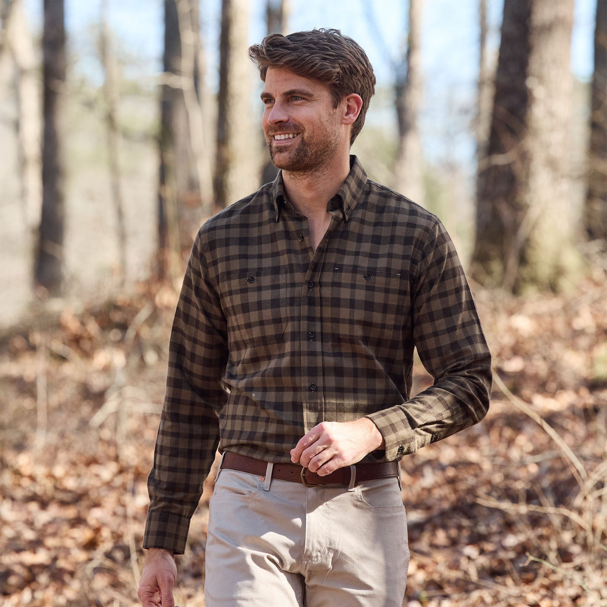 A man in a Tom Beckbe Dixon Brushed Cotton Twill Shirt and beige pants walks outdoors among dry leaves.