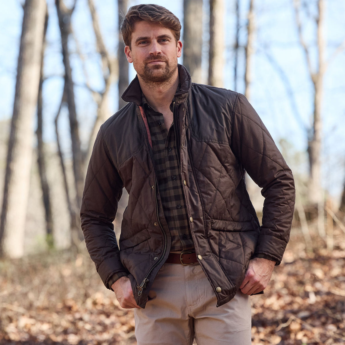 Man wearing a Tom Beckbe Dixon Brushed Cotton Twill Shirt, brown quilted jacket, and khaki pants in the woods.