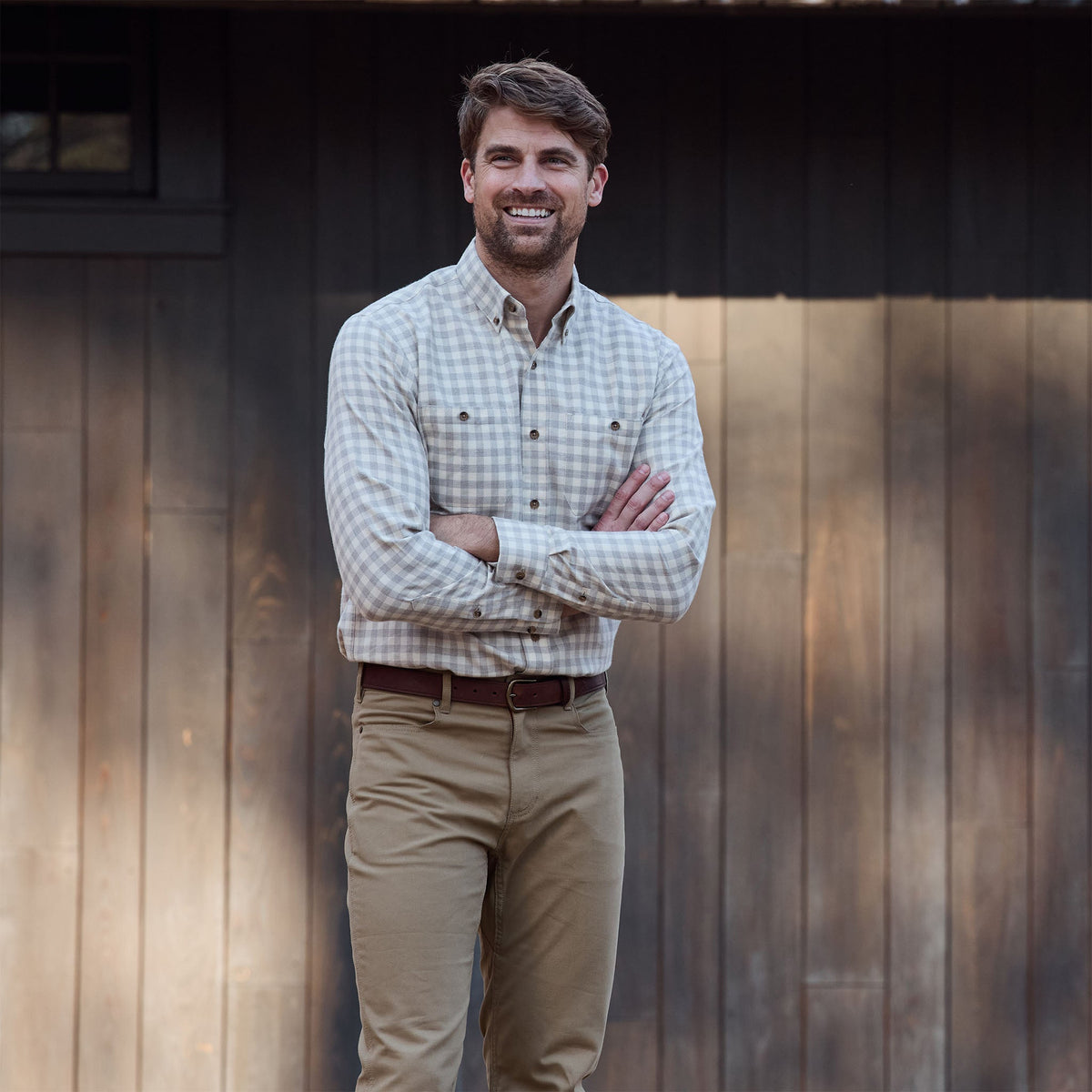 Man outside by wooden wall, smiling with arms crossed, wearing Tom Beckbe Dixon Brushed Cotton Twill Shirt and khakis.