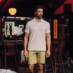 A man in a Tom Beckbe Hutton Performance Polo and khaki shorts stands in a dimly lit bar or restaurant.