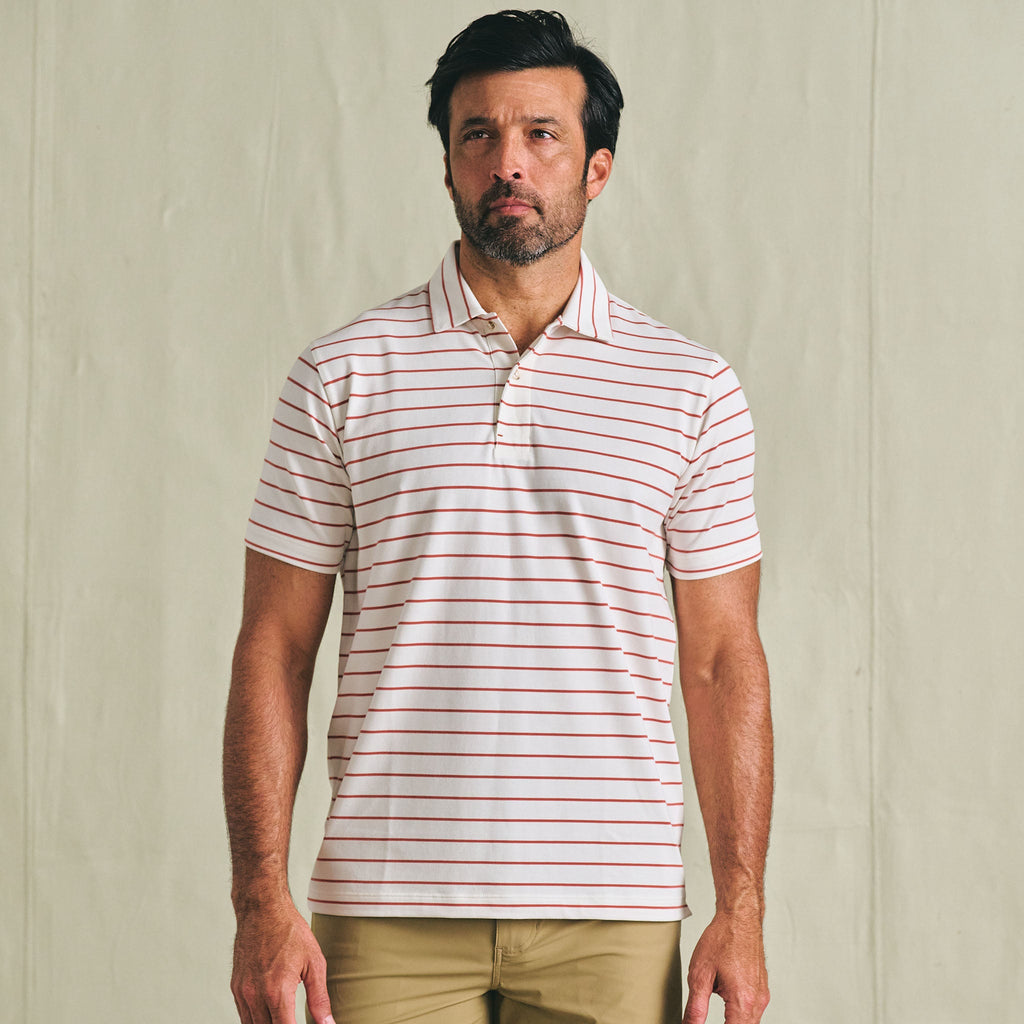 Man wearing a Tom Beckbe Hutton Performance Polo with red stripes and tan pants against a plain background.