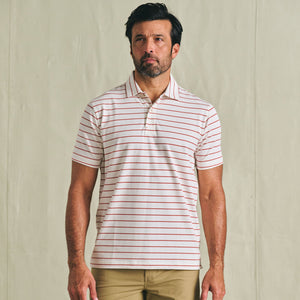Man wearing a Tom Beckbe Hutton Performance Polo with red stripes and tan pants against a plain background.