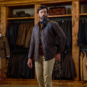 Man wears Tom Beckbe Paddock Quilted Jacket and khaki pants in front of racks with weatherproof jackets and bags.