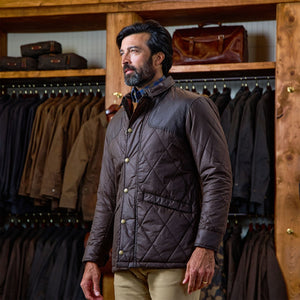 Man wears a Tom Beckbe Paddock Quilted Jacket in a store with weatherproof jackets and bags in the background.