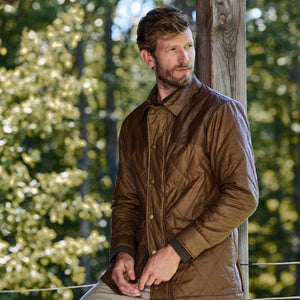 Man in Tom Beckbes Paddock Quilted Jacket leans against a post, showcasing classic outdoor style.