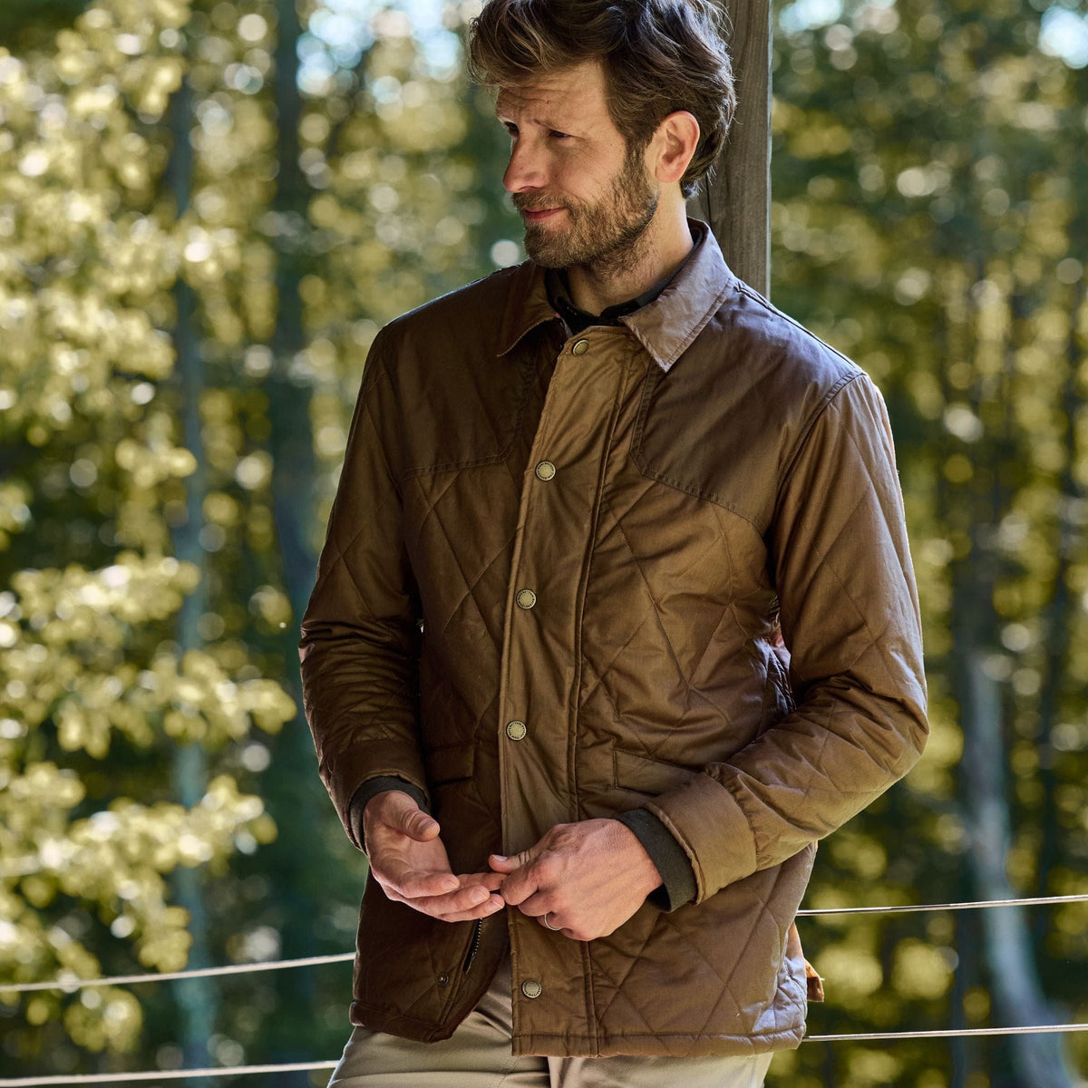 A man outdoors amidst trees wears a Tom Beckbe Paddock Quilted Jacket with breathable insulation.