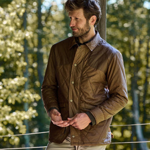 A man outdoors amidst trees wears a Tom Beckbe Paddock Quilted Jacket with breathable insulation.