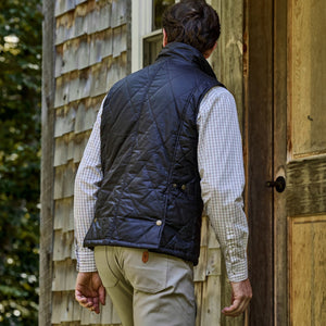 A person in a black Tom Beckbe Paddock Quilted Vest and checkered shirt opens a rustic weatherproof waxed cotton door.