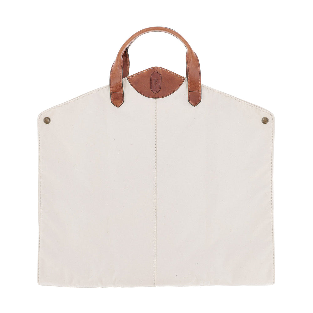 The Tom Beckbe Perdido Canvas Garment Bag features a cream rectangular body, brown leather handles, and metal snap accents.