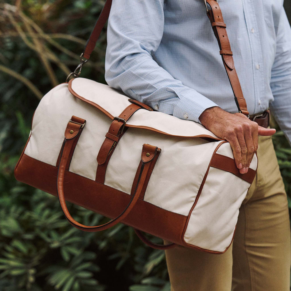 A person in a light blue shirt carries the Tom Beckbe Perdido Canvas Weekender Duffel Bag outdoors.